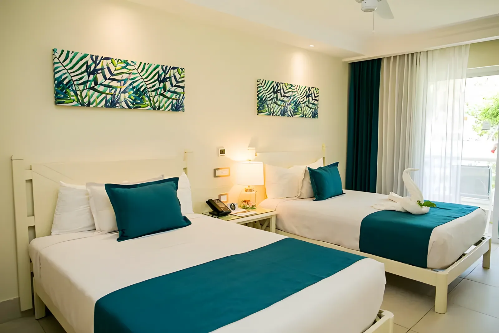 Soba sa dva kreveta, tirkiznim jastucima i tropskom zidnom dekoracijom · Vista Sol Punta Cana Beach Resort & Spa Hotel